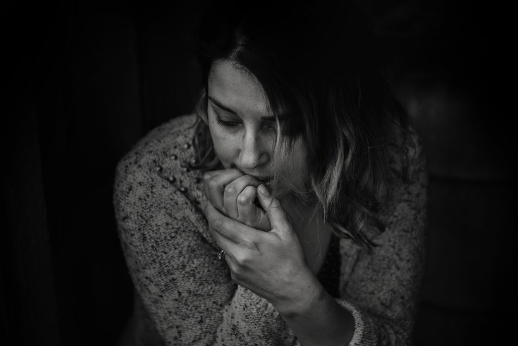 A woman sits in darkness with her hand against her mouth. This could represent the isolation that a trauma therapist in Delray Beach, FL can help you overcome. Learn more about the support a grief counselor can offer by searching "trauma therapy Delray Beach" today.