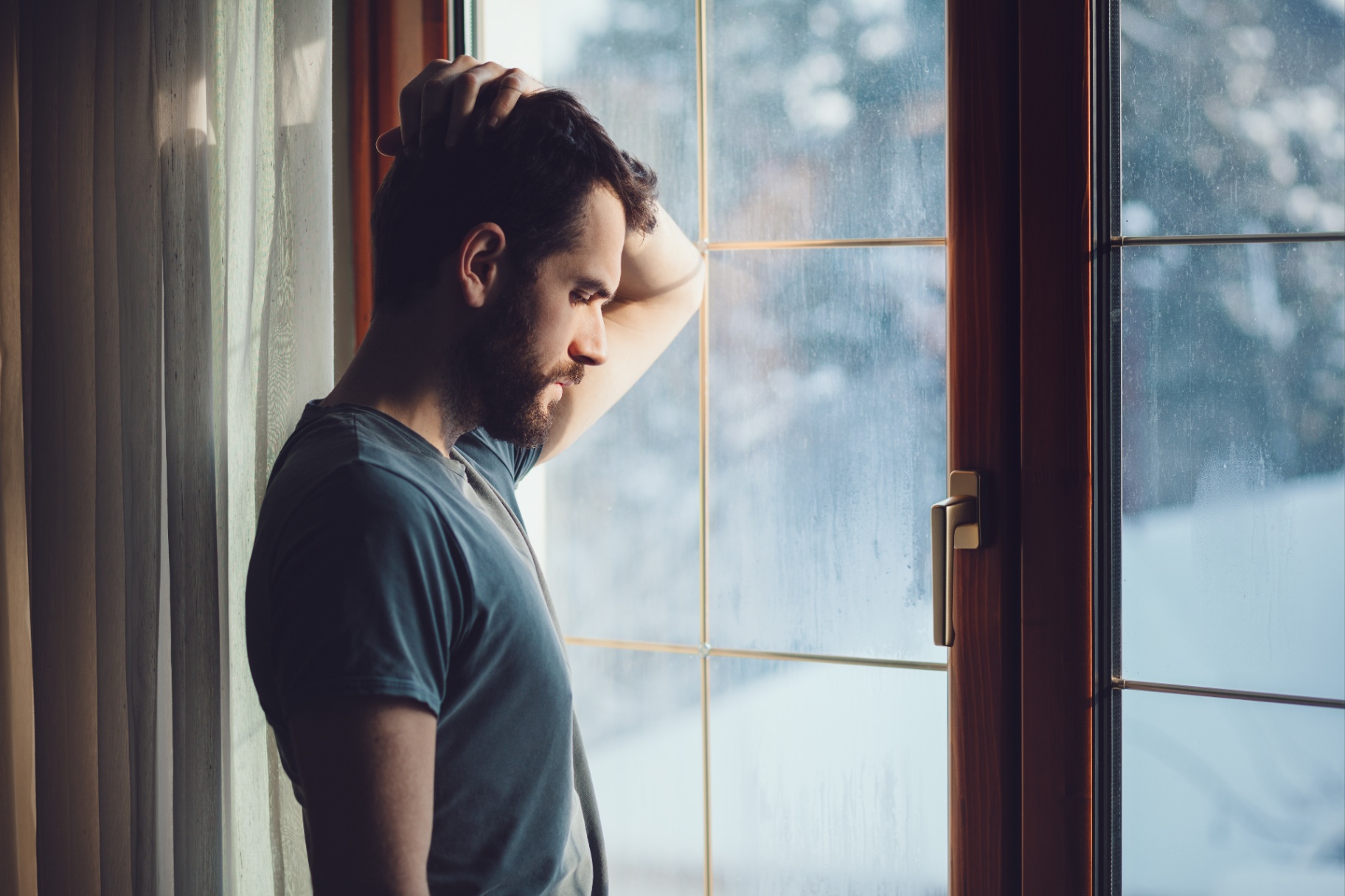 A man holds the back of his head while lookking out a window with a concerned expression. Learn how addiction counseling in Delray Beach, FL can help you overcome isolation and addiction. An addiction therapist in Palm Beach, FL can offer support from the comfort of home with online services.