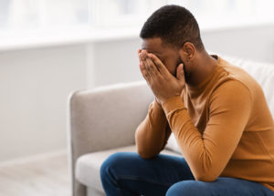 A man covers his face with his hands while sitting on a couch. Learn how trauma treatment in Palm Beach, FL can offer support in overcoming past pain. Contact a trauma therapist in Delray Beach, FL or search "trauma therapy delray beach" to learn more.