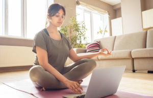 A woman sits in a meditative pose while typing on a laptop. This could symbolize the ease of access to meeting with a trauma therapist in Delray Beach, FL. Learn more about the support an EMDR therapist in Palm Beach, FL can have by searching for trauma treatment in Palm Beach, FL today. 