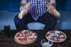A person holds two sub sandwiches in front of pizzas and drinks. Learn more about the support a binge eating therapist in Delray Beach, FL can offer in addressing overeating and binging. Eating disorder treatment in Delray Beach, FL can offer support with an EMDR therapist in Palm Beach, FL.