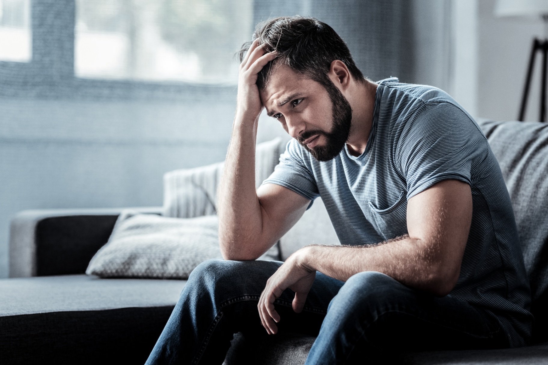A man holds his head with a bleak expression while sitting on a sofa. Learn how eating disorder treatment in Delray Beach, FL can offer support with overcoming past trauma. Contact an EMDR therapist in Palm Beach, FL for support with trauma therapy in Delray Beach, FL. 