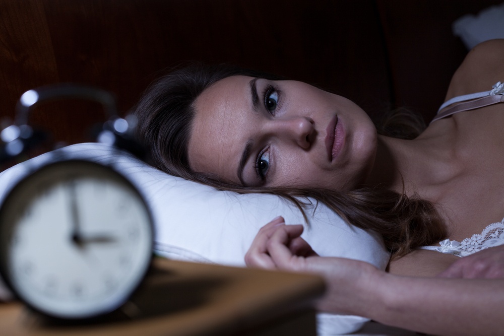 A tired woman lays in bed while looking at her alarm clock. Contact a trauma therapist in Delray Beach, FL to learn more about trauma treatment in Palm Beach County, FL. Learn how CBT-I in Palm Beach County, FL can offer support today.
