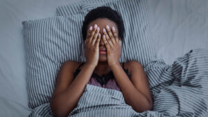 A woman lays in bed covering her face. This could represent the pain of insomnia an EMDR therapist in Palm Beach County, FL can offer support in addressing. Learn more from a trauma therapist in Delray Beach, FL or search for CBT-I in Palm Beach County, FL today. 