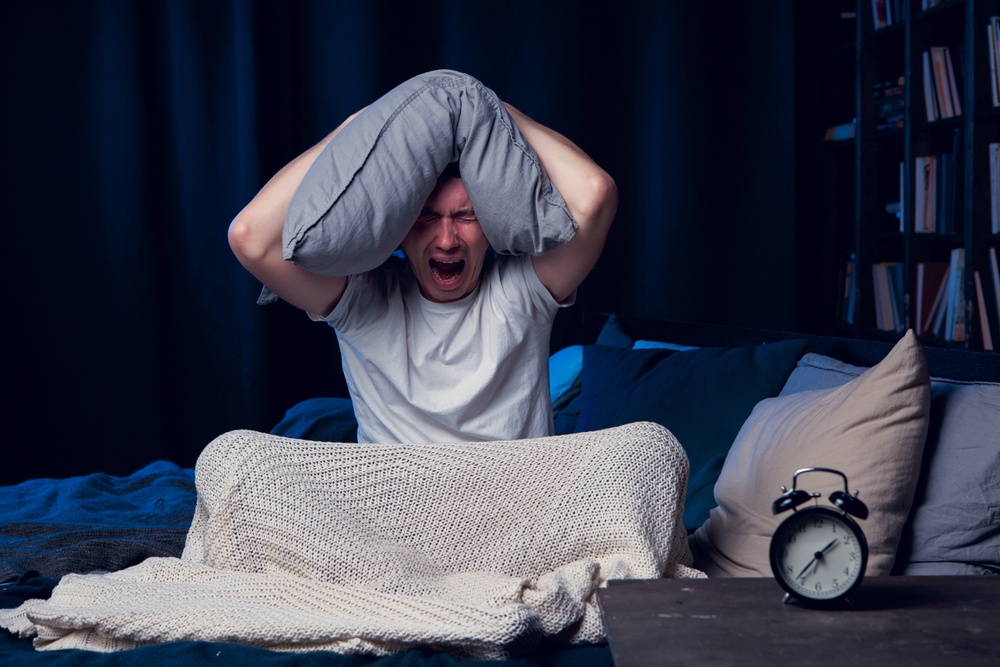 A man yells in bed while holding a pillow over his head. Learn how CBT-I in Palm Beach County, FL can offer support in addressing insomnia and trauma. Learn more from a trauma therapist in Delray Beach, FL, or search for trauma treatment in Palm Beach County, FL today. 