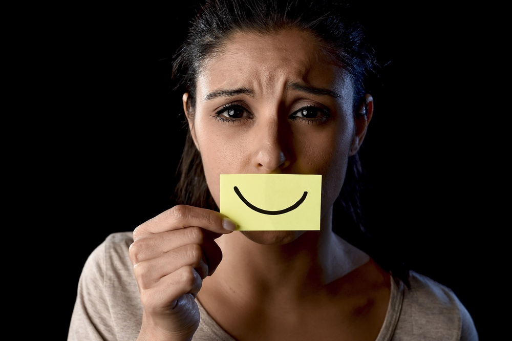 A woman appears to be upset while holding a smiley face post it in front of her mouth. Learn how to overcome masking with the help of anxiety treatment in Palm Beach County, FL. Search for an anxiety therapist in Palm Beach County, FL or search for online therapy in Florida for remote support. 