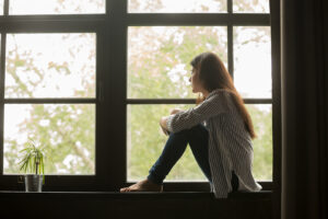 A woman sits in a windowsill while looking outside with a stressed expression. Learn how an anxiety therapist in Palm Beach County, FL can offer support by searching for EMDR in Palm Beach County, FL today. Search for anxiety treatment in Palm Beach County, FL for more info today. 