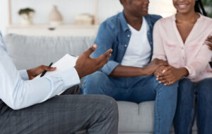 A person gestures with their hand while sitting across from a smiling couple. This could represent the support a therapist in Palm Beach County, FL can offer. Search for a therapist in Delray Beach, FL or online therapy in Florida today. 