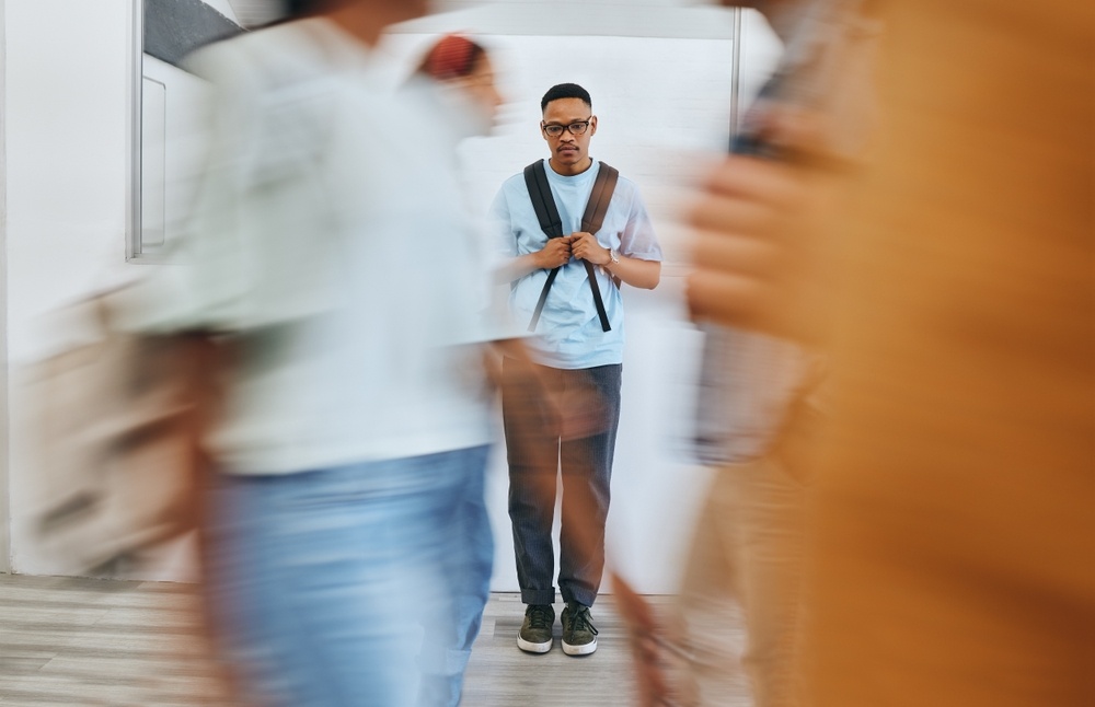 A student stands with an anxious look while people walk across a hallway. This could represent the social stress from anxiety that an EMDR therapist in Palm Beach County, FL can offer support with addressing. Contact an EMDR therapist in Palm Beach County, FL for online anxiety treatment in Delray Beach, FL today.