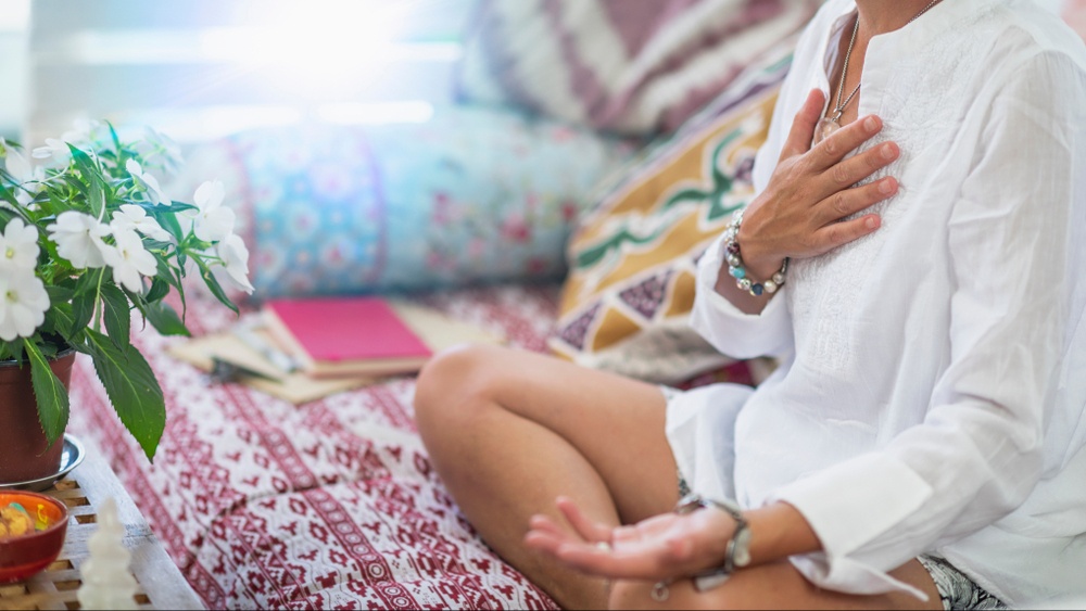 A close up of a person touching their chest while sitting on a cushion and doing a breathing exercise. This could represent a coping technique learned from a trauma therapist in Delray Beach, FL. Learn more about trauma therapy in Delray Beach, FL today. 