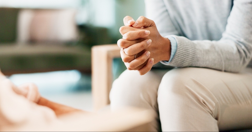 A close up of a person sitting with their hands gother while sitting across from a person listening. This could represent the support a trauma therapist in Delray Beach, FL can offer. Search for trauma treatment in Palm Beach County, FL today. 