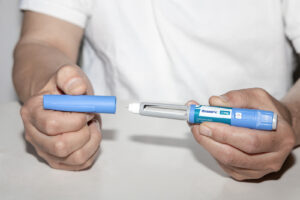 A close up of a person holding an Ozempic injection while taking off the cap. This could represent the benefits of using weight loss drugs in addition to mental health support search for a binge eating therapist in Delray Beach, FL and how they can offer Palm Beach County, FL therapy today. Search for eating disorder treatment in Delray Beach, FL today for more info.